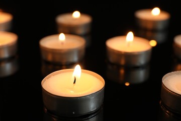 Many burning tealight candles on black background, closeup