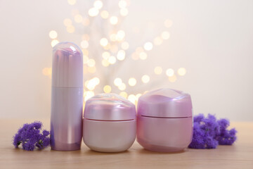 Set of different cosmetic products and ageratum flowers on wooden table against light background with blurred lights