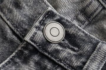 Close-up of a metal button on black denim jeans. Detailed view of a round metallic button fastened...