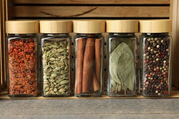 Different spices in glass jars on grey wooden table, closeup