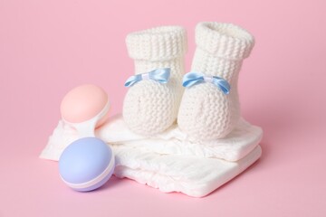 Baby rattle, booties and diapers on pink background