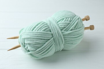 Plush yarn with knitting needles on white wooden table, closeup