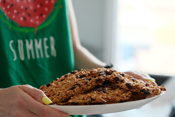 A person holding a plate of homemade oatmeal cookies, wearing a green summer-themed shirt with a watermelon graphic