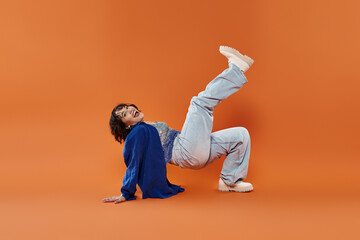 A woman wearing a blue shirt and jeans laughs while posing on a bright orange background.