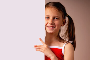 Cheerful young girl behind white blank banner and empty copy space advertisement board on brown background. Copy space for text or design.