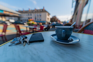 A cup of expresso coffee on an outside table in a cafe with glasses, key ring and mobile phone, shot with a very wide angle and shallow depth of field