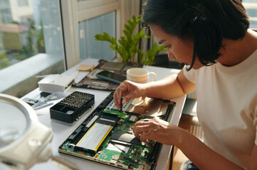 Young woman using screwdriver in repair of laptop in workshop