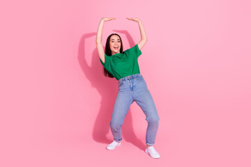 Full length photo of adorable lovely girl wear green t-shirt pushing arms up empty space isolated pink color background