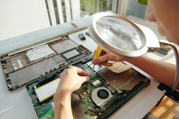 Close-up of repairman screwing the board of laptop under magnifier at his workplace
