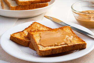 Toast bread and Homemade peanut butter.Spreading peanut butter on slice whole wheat bread in white plate.