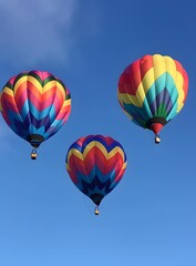 Fototapeta premium Three Colorful Hot Air Balloons Against Blue Sky