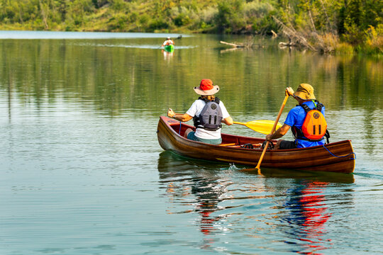 Female and male canoeist on a lake paddling with refection in the lake; Calgary, Alberta, Canada