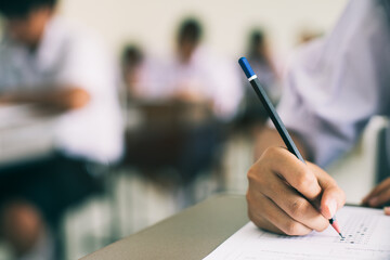 Close up hand of student reading and writing exam answer sheets exercises with stress in classroom