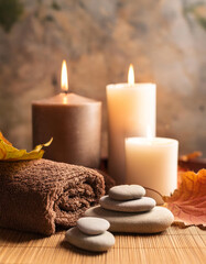 Cozy spa setting with candles, smooth stones, soft towels and autumn leaves on warm wooden surface. Relaxation and meditation. Wellness, body and healthcare.