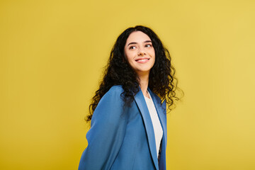 A young, brunette woman in a blue jacket stands confidently in front of a striking yellow wall, exuding style and emotion. © LIGHTFIELD STUDIOS