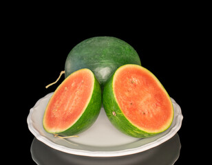 Two juicy watermelon halves and one whole on a white ceramic dish, macro, isolated on black...