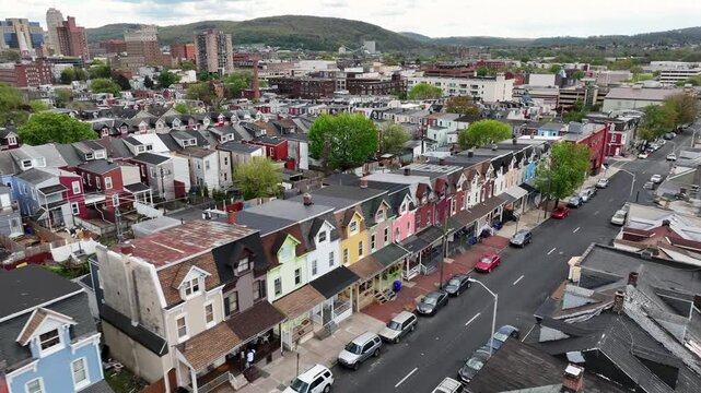 Aerial approaching flight along street with colorful house front in suburb of american town. Row of small houses in suburbia. Downtown towers in background. Wide shot.