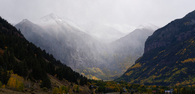 Scenic view through fall colored mountain slopes of snow-capped mountain peaks covered in misty fog; near Aspen, Colorado, United States of America