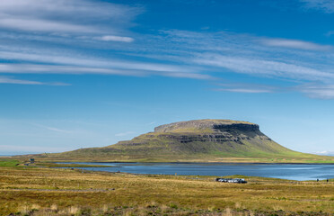 Majestic hill by serene lake and green meadows under vivid blue sky