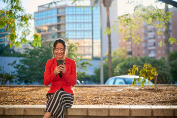 Asian businesswoman using smartphone while sitting in a city park