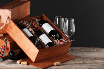 Box with wine bottles and glasses on wooden table against black background. Space for text