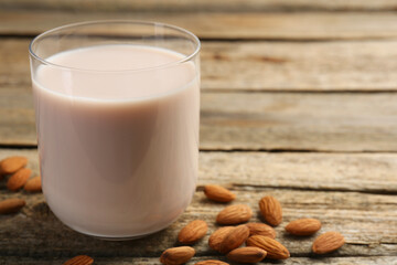 Glass of almond milk and almonds on wooden table, space for text