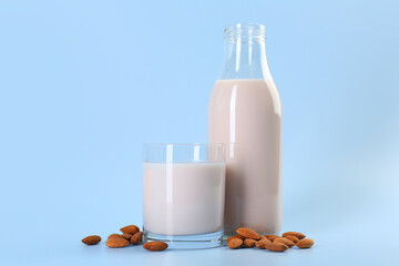 Fresh almond milk in bottle, glass and nuts on light blue background, space for text