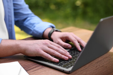 Freelancer working with laptop at wooden table outdoors, closeup. Remote job