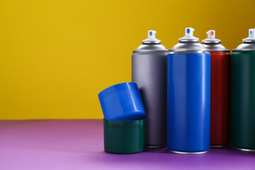 Many spray paint cans on color background, space for text