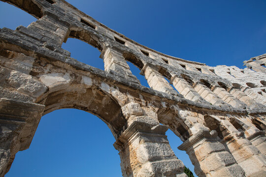 Close-up view of a section of the stone structure of the ancient Roman Amphitheater, the Pula Arena against a blue sky, constructed in 27 BC - AD 68; Pula, Croatia