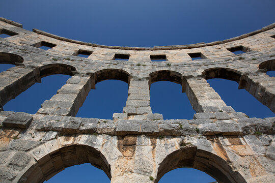 Close-up view of a section of the stone structure of the ancient Roman Amphitheater, the Pula Arena against a blue sky, constructed in 27 BC - AD 68; Pula, Croatia