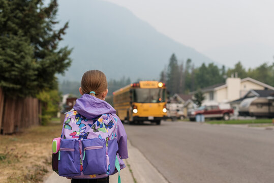 Little girl with backpack waits for bus on first day of school.
