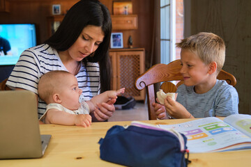 Young mother helping children with homework and snack time