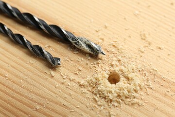Drill bits and sawdust on holed wooden surface, closeup