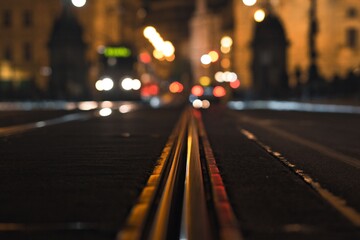 Close-up of tram tracks in a city at night with blurred lights and buildings in Prague
