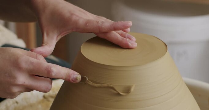 Handheld shot of doing pottery, creating the bottom of a bowl with a special tool. Hands removing clay.