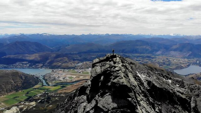 Mountaineer standing ontop of high rocky mountain overlooking Queenstown and Lake Wakatipu in New Zealand.
