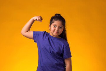 Kid girl showing winner or strength gesture over yellow background. Success, victory and good health concept