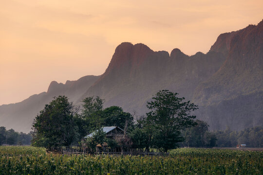 Countryside with farmland at twilight surrounded by silhouetted karst formations in the Kong Lor Cave area of Laos; Khammouane Province, Laos