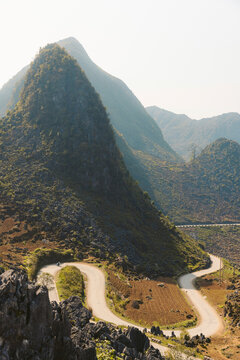 Road with switchback curves winding through a valley with peaked mountains in the countryside of Vietnam; Bao Tang Con Duong Hanh Phuc, Meo Vac District, Ha Giang, Vietnam