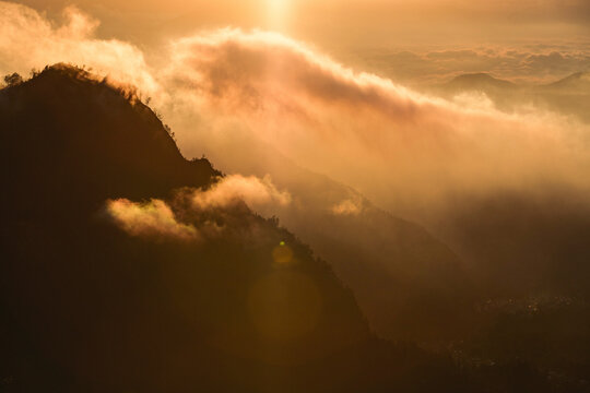 Bright golden sunlight illuminates the clouds over mountains in Bromo Tengger Semeru National Park, East Java, Indonesia; Ranupani, East Java, Indonesia