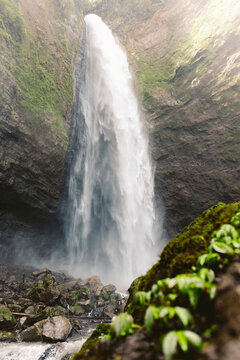Motion blur and dramatic splashes from a high waterfall and lush vegetation at Air Terjun Kabut Pelangi, Indonesia; Kecamatan Pronojiwo, Kabupaten Lumajang, Jawa Timur, Indonesia