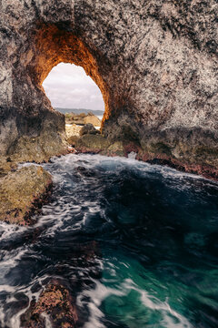Surf flowing towards a natural arch along the beautiful rugged coastline of Central Sulawesi, Indonesia; Tanjung Gundul Pasir Putih, Banggai Islands Regency, Central Sulawesi, Indonesia