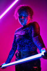 A striking African American woman wields a LED lamp in a dimly lit room.