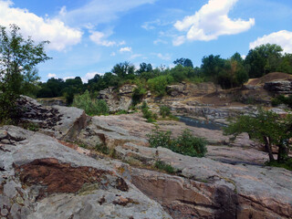 A picturesque abandoned granite quarry overgrown with green grass and trees. A great place for hiking and active recreation