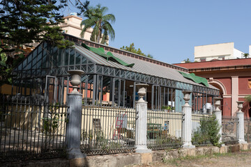 A glass enclosed greenhouse with a metal frame sits behind a wrought iron fence