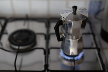 A silver coffee pot sits on a stovetop burner with a blue flame underneath