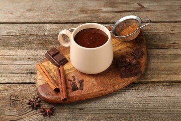 Tasty melted chocolate in cup and spices on wooden table