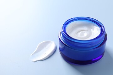 Face cream in jar and smear on light blue background, closeup. Space for text