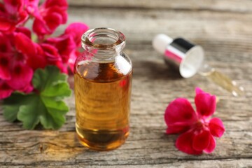 Bottle of geranium essential oil, pipette and beautiful flowers on wooden table, closeup